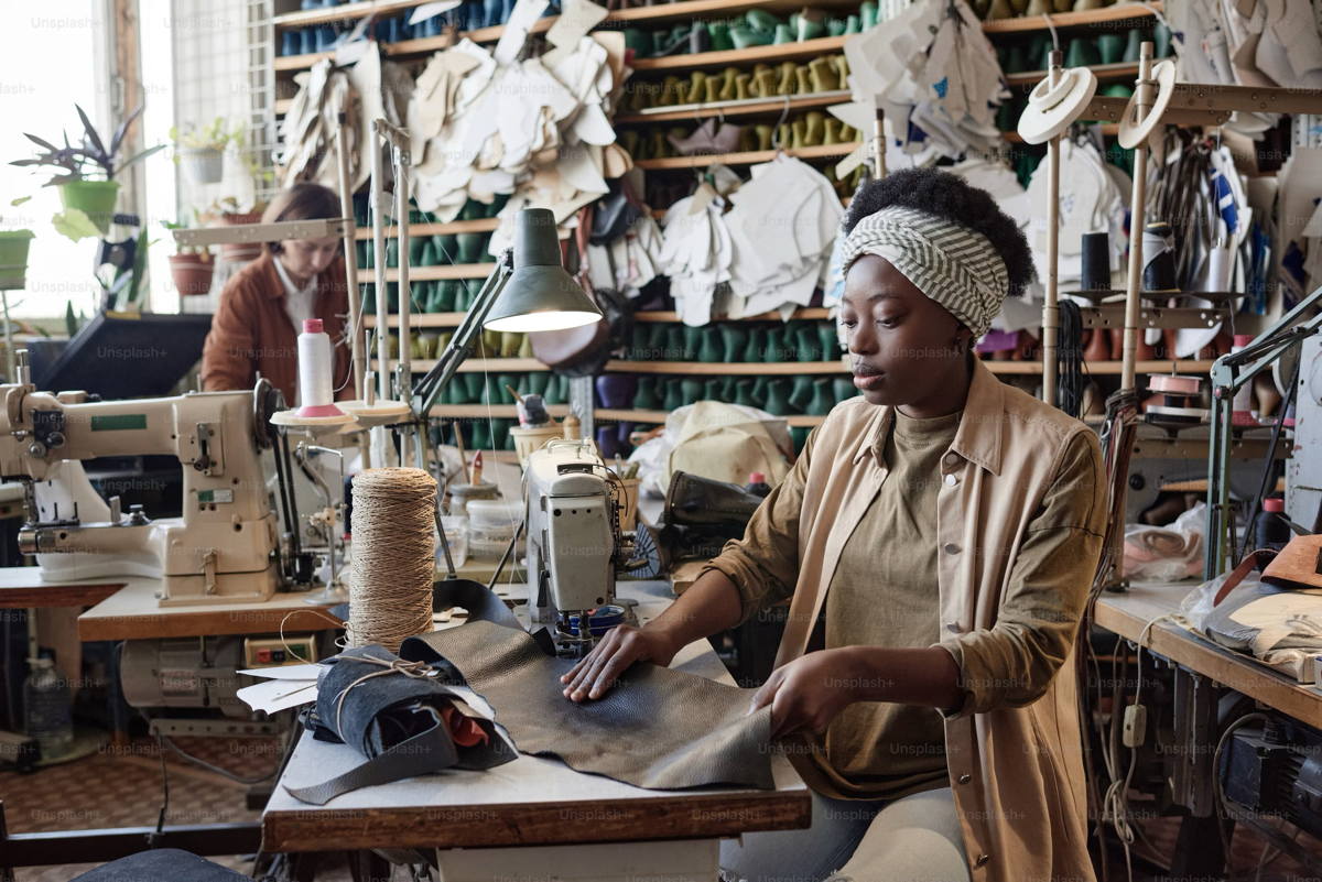 african-tailor-sitting-at-her-workplace-with-sewing-machine-and-sewing-products-in-factory